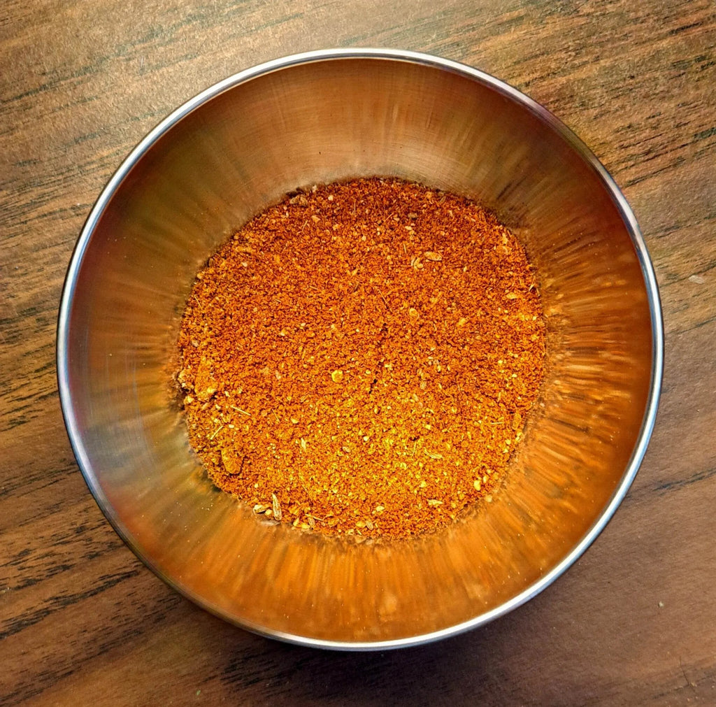 Metallic bowl filled with a Chili Powder spice mix on a wooden surface
