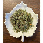 Diuretic Tea herbal blend on a white leaf shaped ceramic dish on a wooden surface.