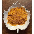 Golden Milk Latte powder in a white leaf-shaped bowl on a wooden surface