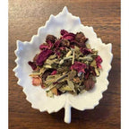 White leaf-shaped bowl filled with Happy Heart tea mix on a wooden surface
