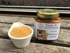 Jar of Triple H Country Essentials Mustard Caviar on a wooden surface with mustard seeds.