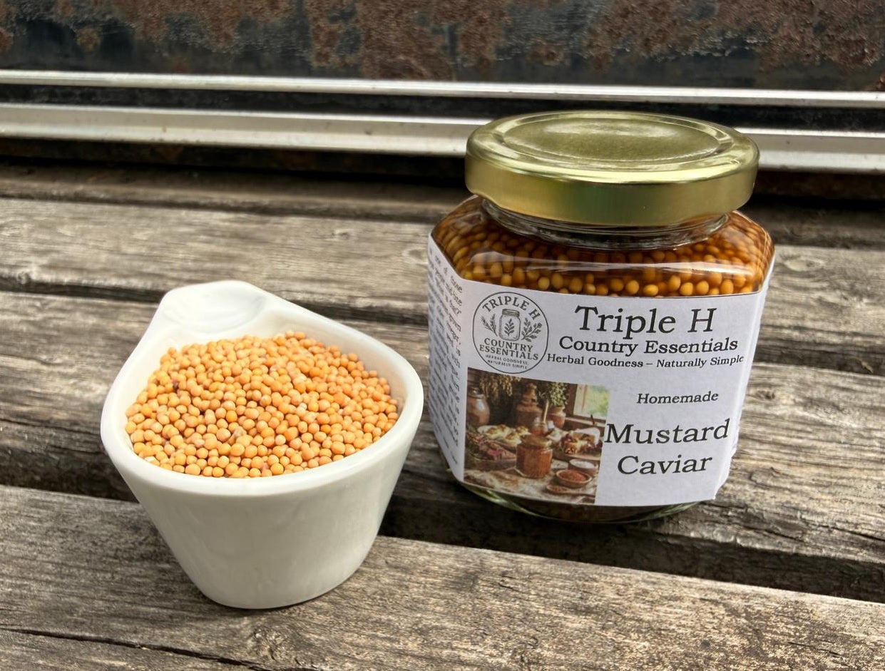 Jar of Triple H Country Essentials Mustard Caviar on a wooden surface with mustard seeds.