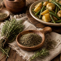 A wooden spoon filled with dried savoury sits on a rustic table beside fresh savoury sprigs, with cooked potatoes and green beans in a bowl in the background.